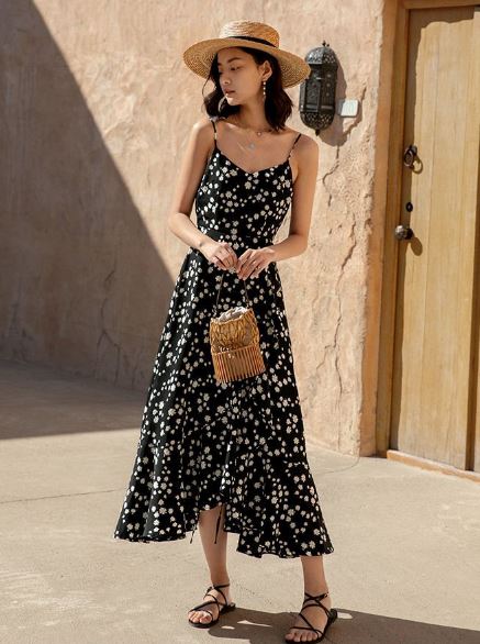 robe longue à fleurs noire aliénor pour été avec bretelles fines et chapeau de paille, et une femme en extérieur