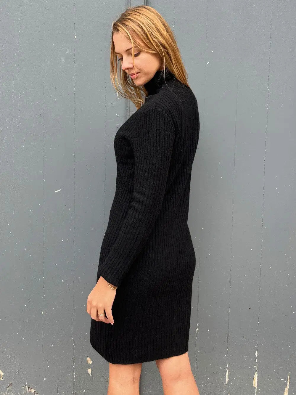 femme portant une robe pull col roulé en cachemire noir avec un sac en bandoulière à côté d'un mur texturé