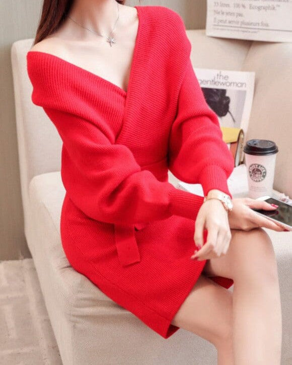 Femme portant une robe pull cache coeur rouge assise sur un canapé blanc avec une tasse de café sur la table.