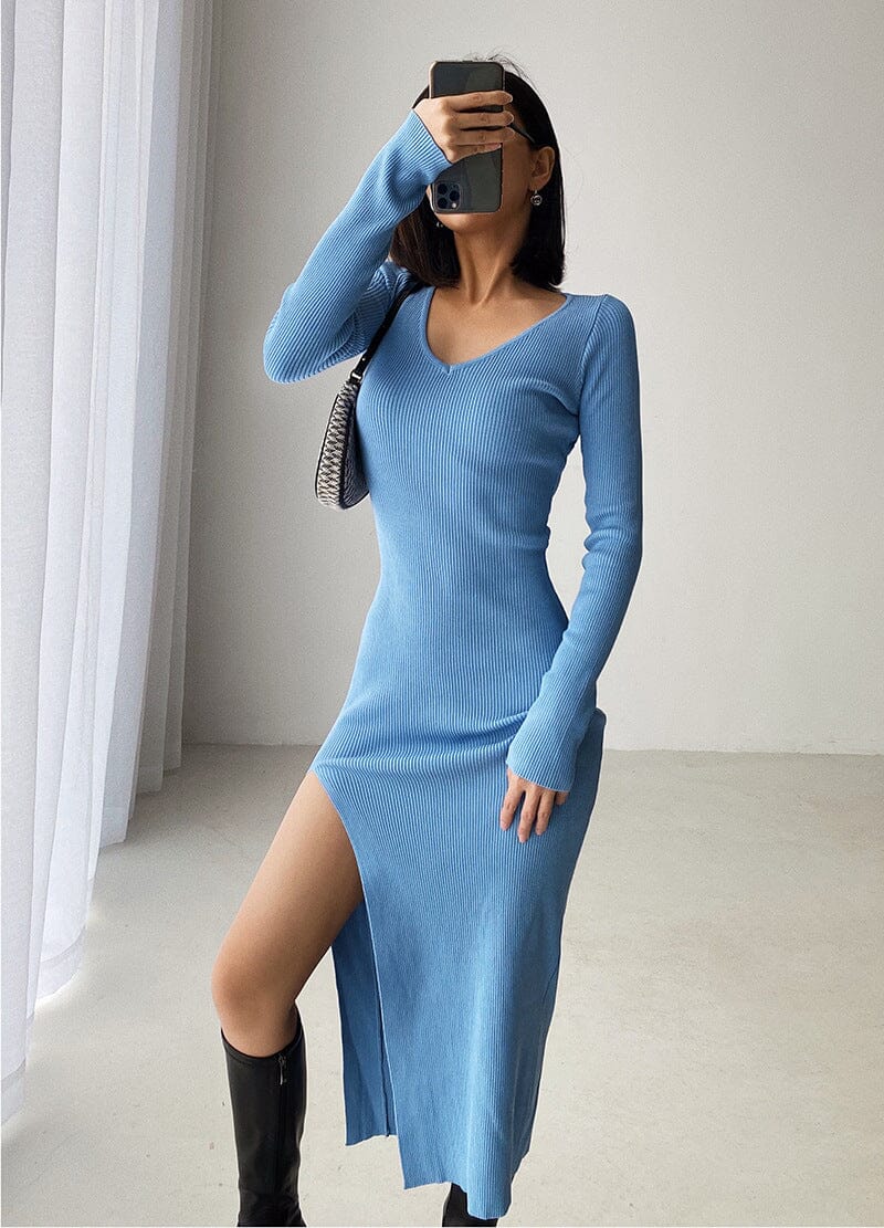 Femme posant avec une robe pull longue bleue à manches longues, fente élégante et col en V, style moderne et chic.