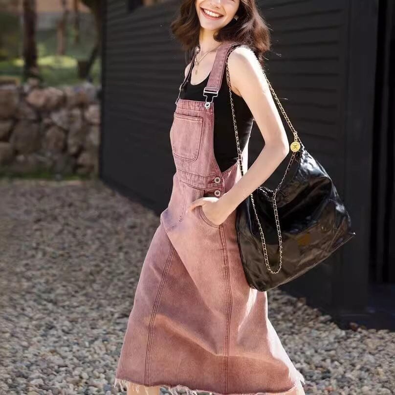 robe salopette en jean mona portée par une femme souriante, avec un grand sac noir en bandoulière, devant une maison noire