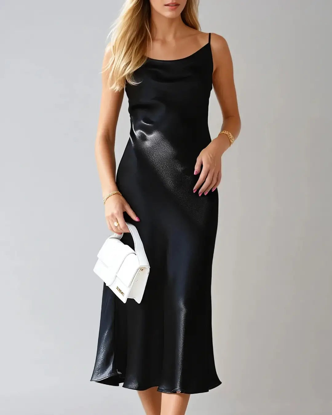 Robe cocktail en satin Victorine avec fines bretelles, élégante et fluide, portée par une femme tenant un sac blanc.