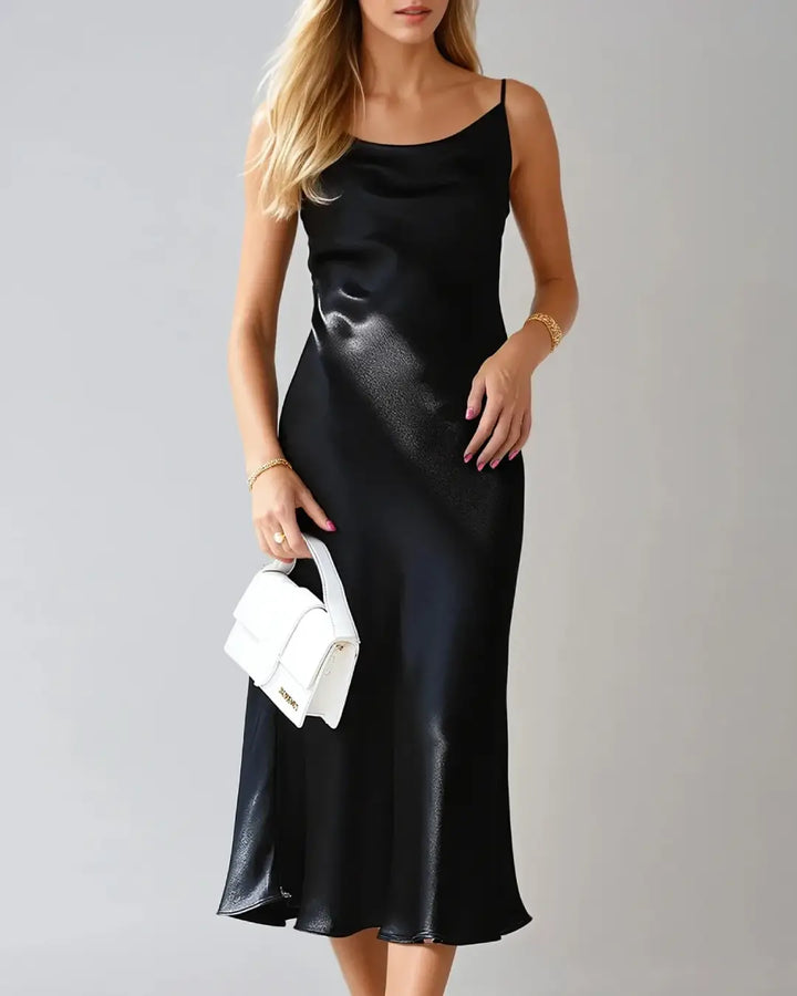 Robe cocktail en satin Victorine avec fines bretelles, élégante et fluide, portée par une femme tenant un sac blanc.