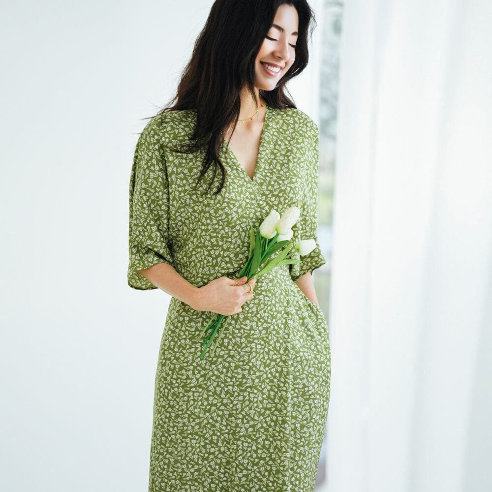 robe longue fluide fleurie coline avec motif floral vert portée par une femme tenant des fleurs dans un décor lumineux