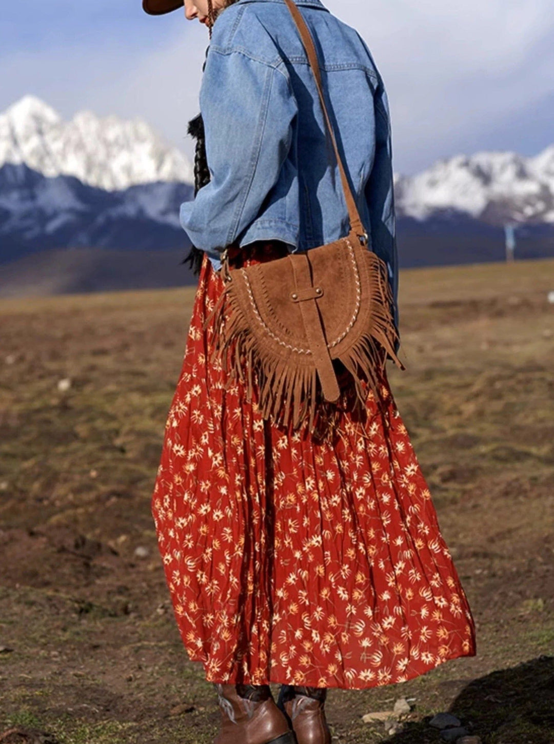 sac en daim frangé porté par une femme en extérieur, avec une jupe longue rouge et une veste en jean, fond montagneux