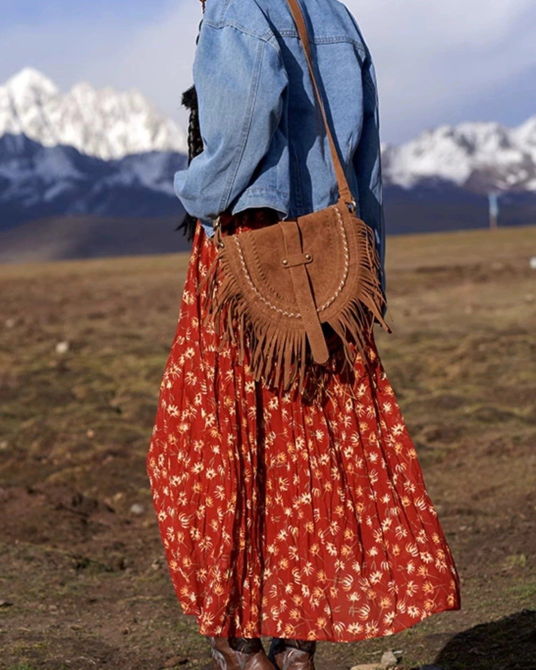 sac en daim frangé porté par une femme en extérieur, avec une jupe longue rouge et une veste en jean, fond montagneux