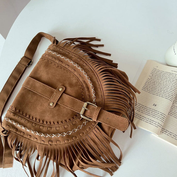 sac en daim frange marron avec détails en cuir et broderies blanches, posé sur une table blanche à côté d'un livre ouvert