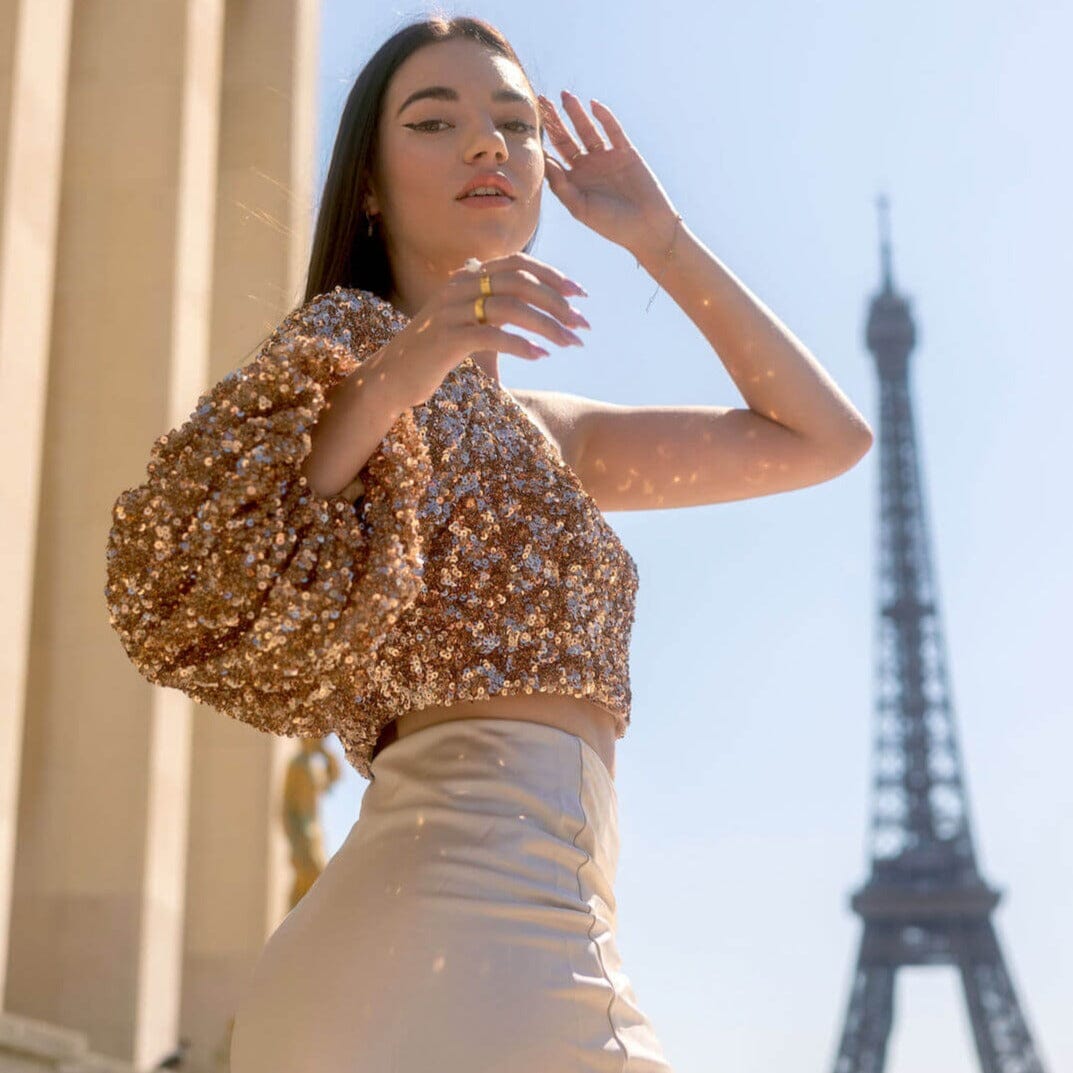 femme portant un top sequin doré devant la tour eiffel, édition limitée. haut pailleté élégant pour soirée à paris