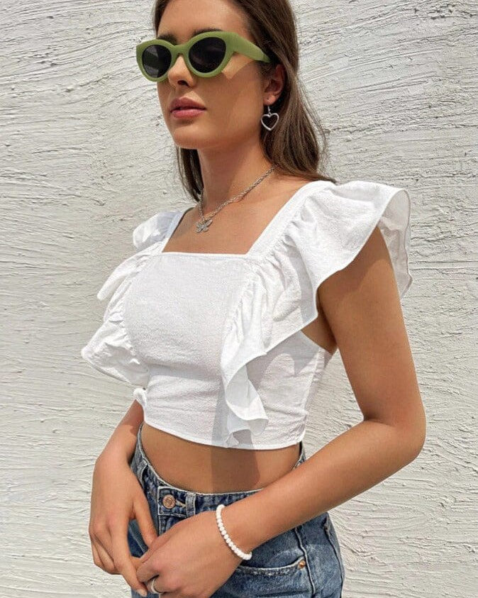 jeune femme portant un top dos nu volanté ariane en blanc avec des lunettes de soleil vertes et un jean casual