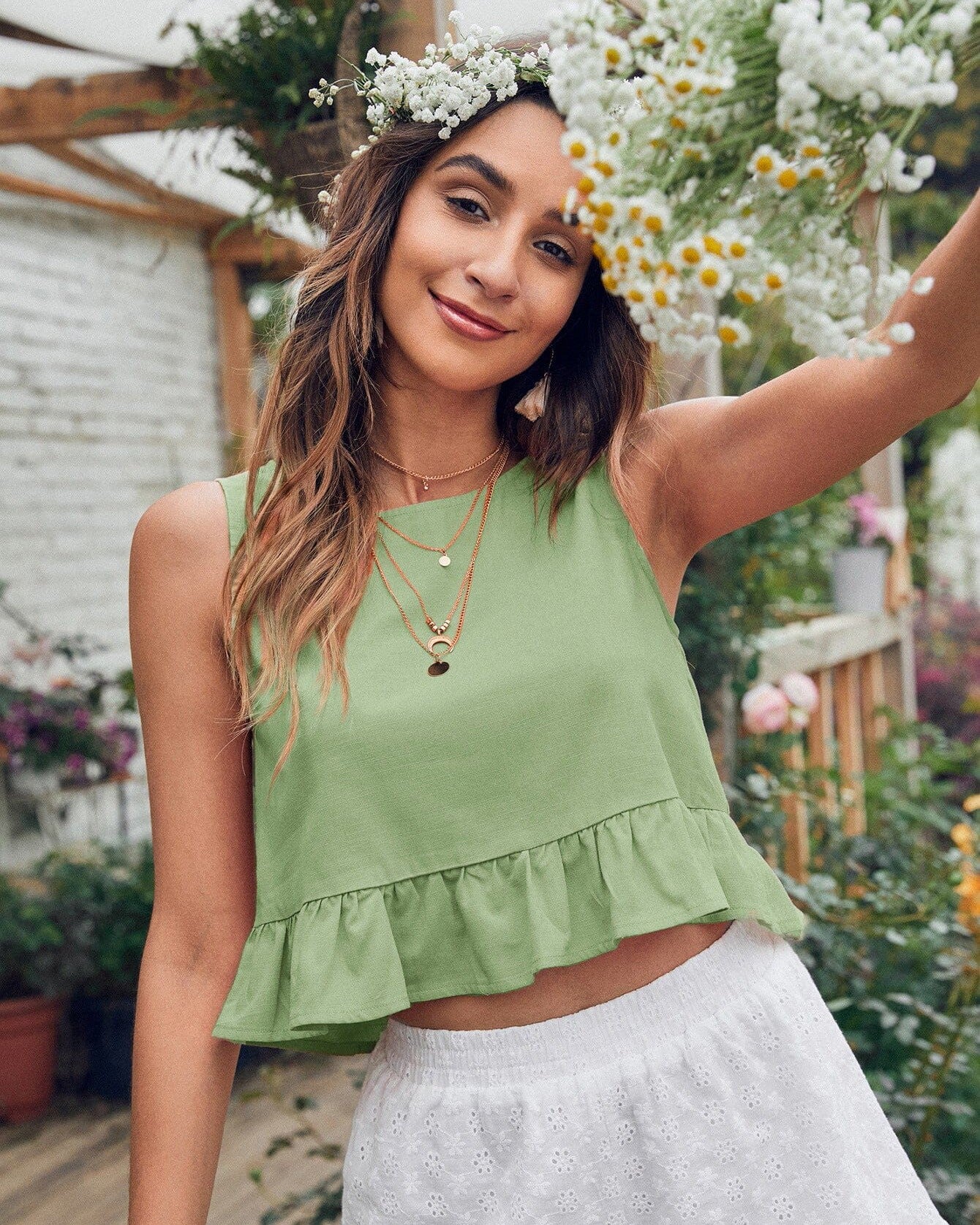 femme portant un top peplum vert vika en dentelle dans un jardin fleuri, accessoirisé avec des colliers dorés et une couronne de fleurs