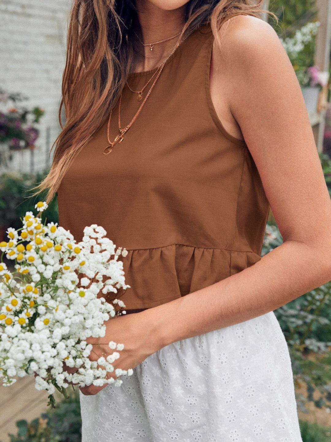 top peplum sans manches de couleur marron porté par une femme tenant un bouquet de fleurs blanches, devant un jardin