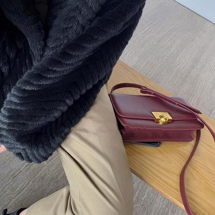 veste femme fausse fourrure chic noire avec un sac à main bordeaux reposant sur une table en bois et un pantalon beige