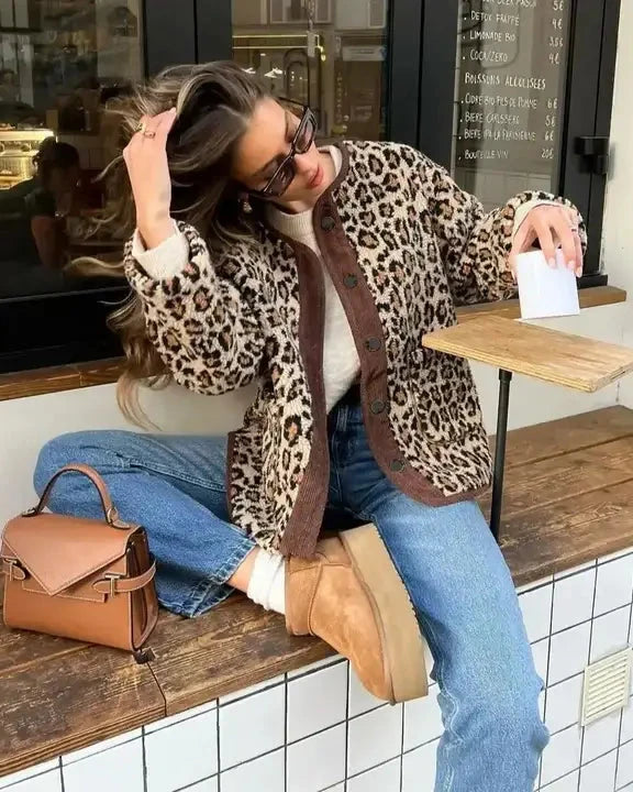 Femme portant une veste en polaire léopard Edna assise près d'une fenêtre avec un sac à main en cuir marron.