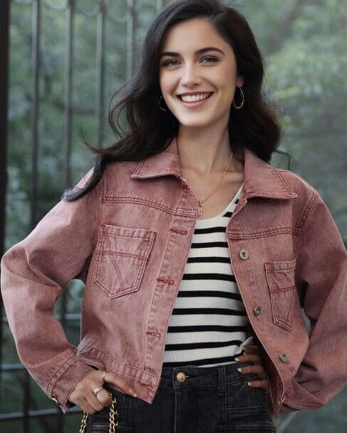 femme portant une veste en jean courte carrie de couleur rose avec un t-shirt rayé noir et blanc, souriante en extérieur