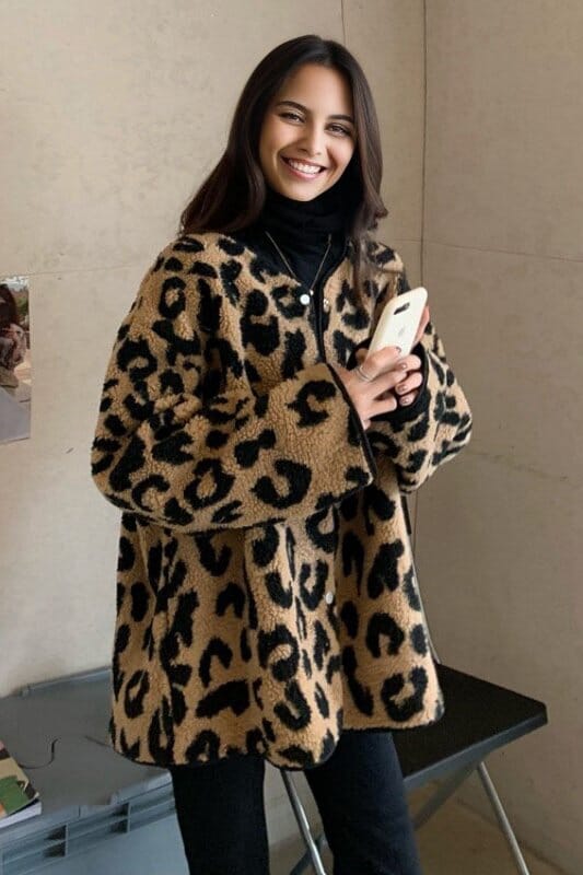 Femme souriante portant une veste en sherpa motif léopard, confort et style moderne pour temps frais.