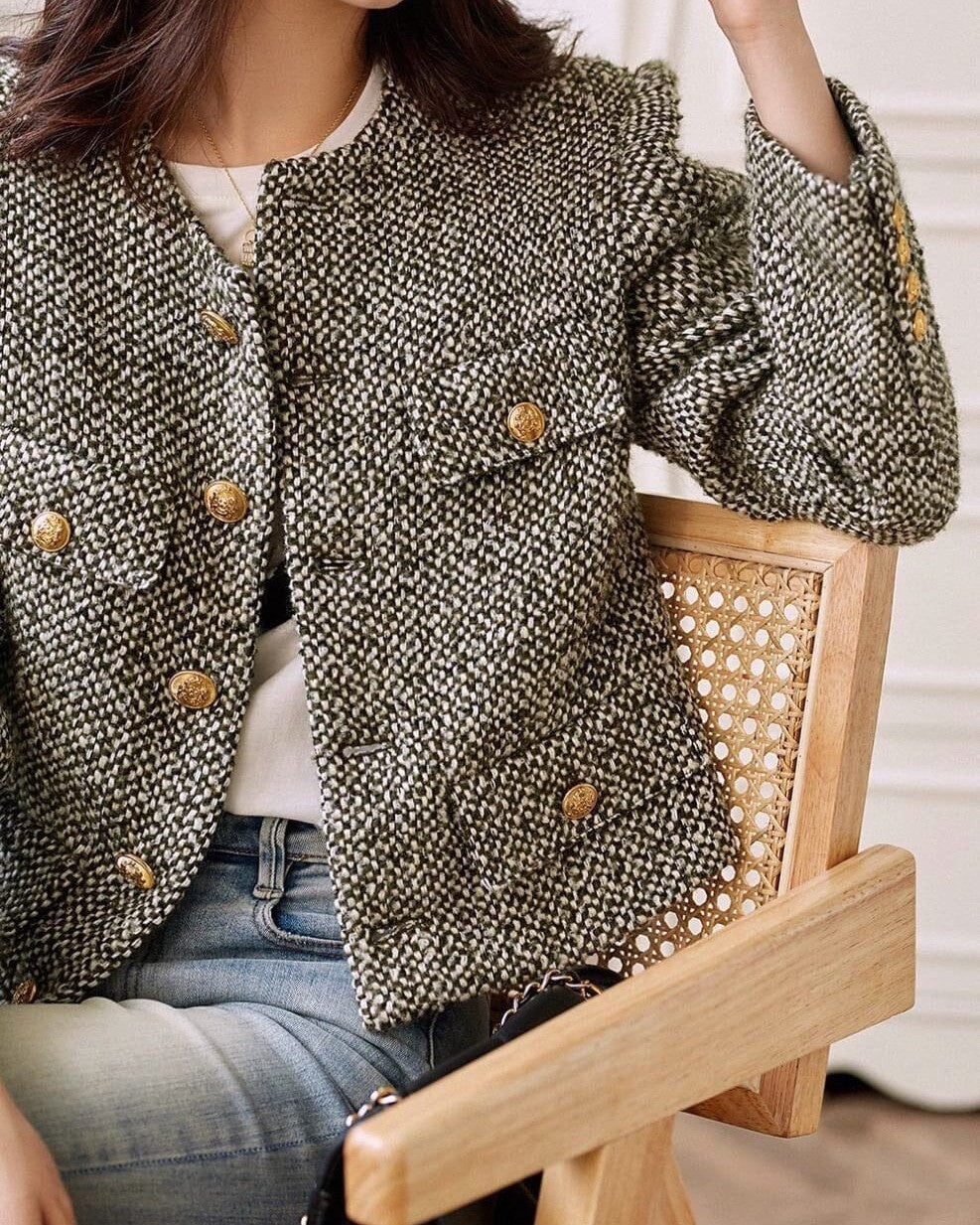 veste en tweed femme avec boutons dorés, assise sur une chaise en bois, look élégant avec jeans bleus casual