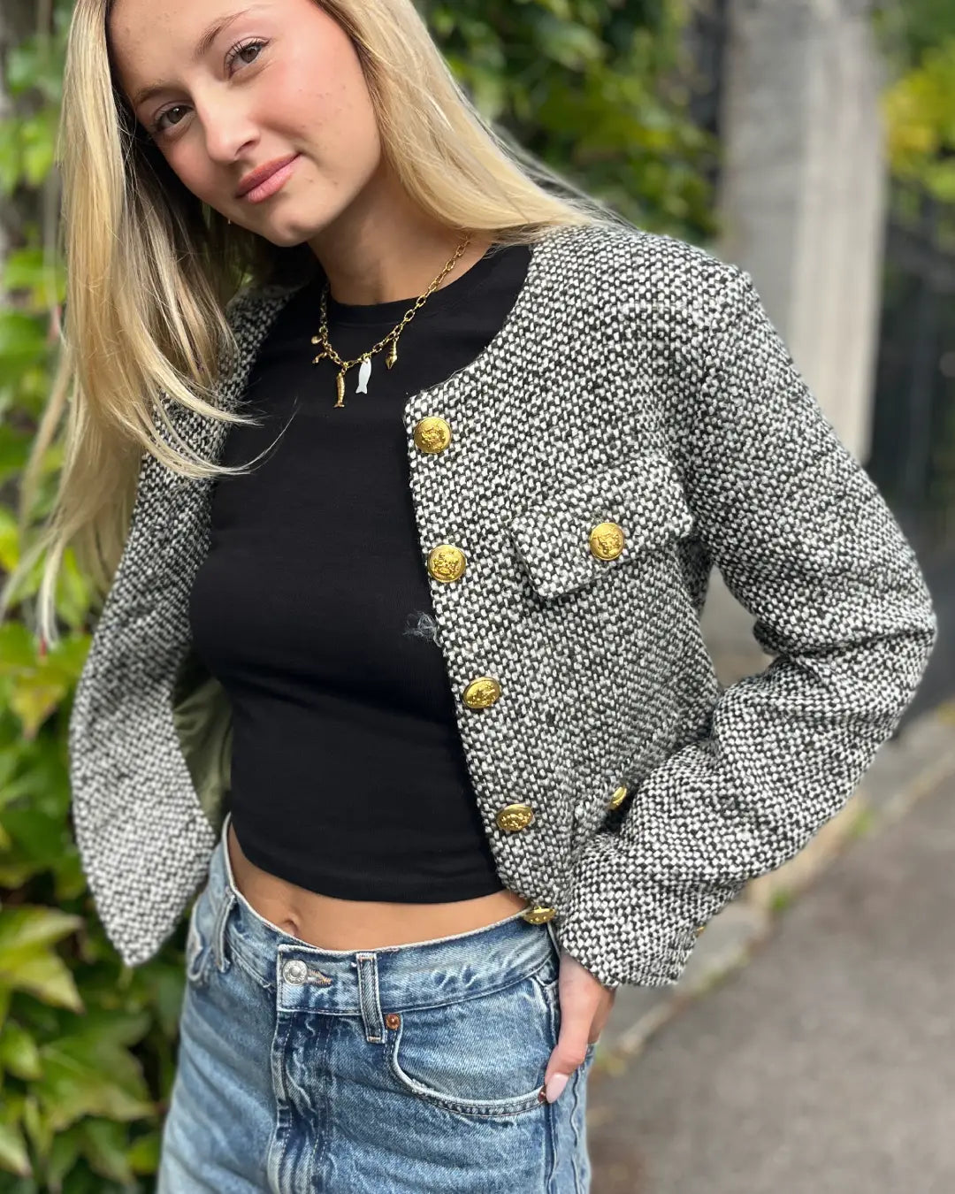 Veste en tweed élégante pour femme avec boutons dorés, portée sur un top noir et jean décontracté, look automnal moderne.