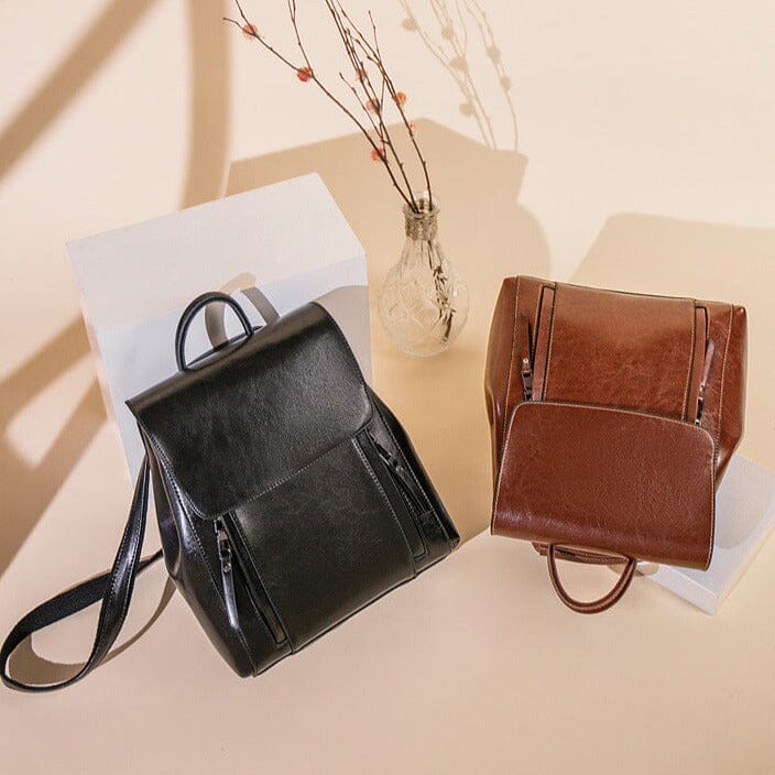 deux sacs à dos en cuir, noir et marron, posés sur des boîtes blanches avec une décoration minimaliste en arrière-plan