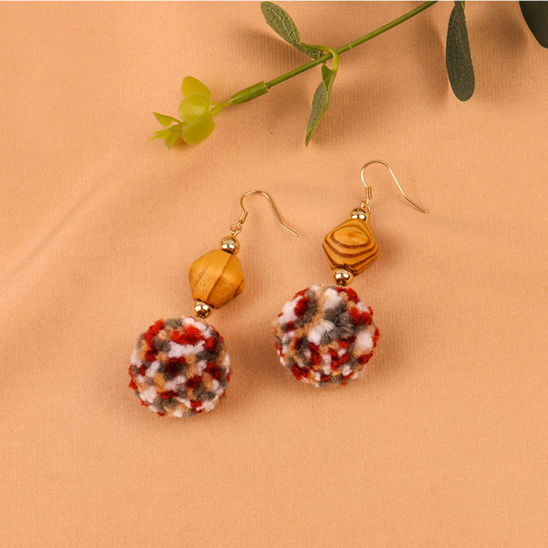 boucles d'oreilles pompon multicolore avec perles en bois sur fond beige, accessoire féminin coloré et élégant
