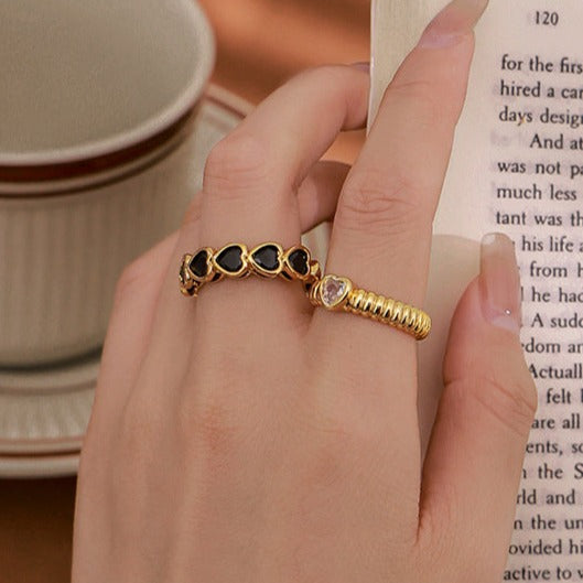 bague dorée ajustable avec motif cœur portée sur une main tenant un livre à côté d'une tasse de café sur une table