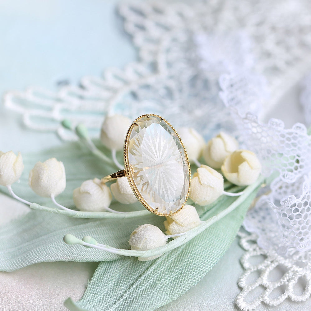 bague plaqué or pour femme ornée d'un cristal transparent sur fond décoratif de fleurs et dentelle blanche
