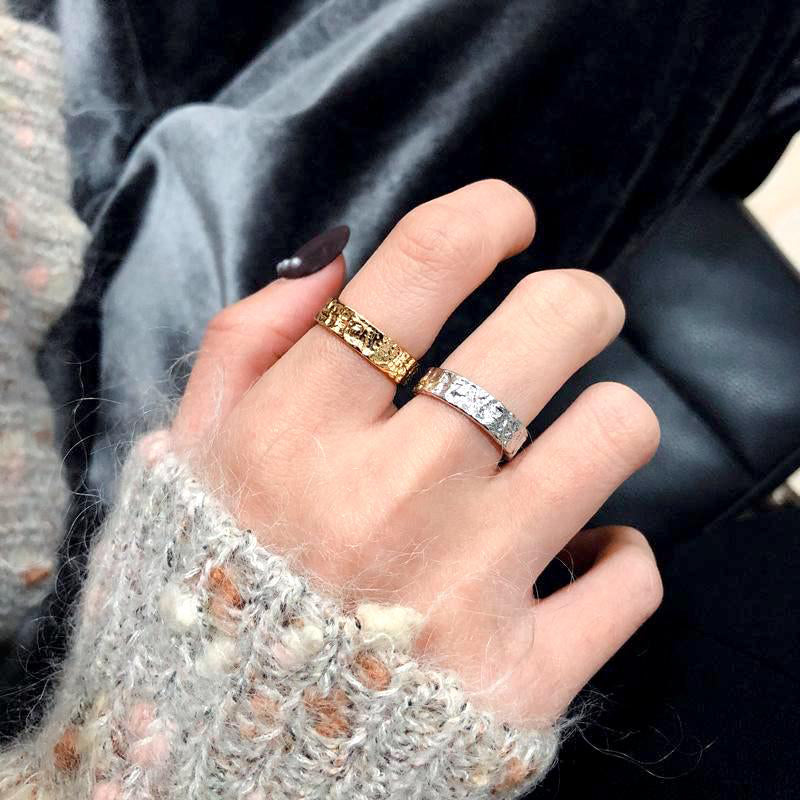 bague de femme avec textures en relief, une dorée et une argentée, portée sur un doigt d'une personne avec un pull tricoté