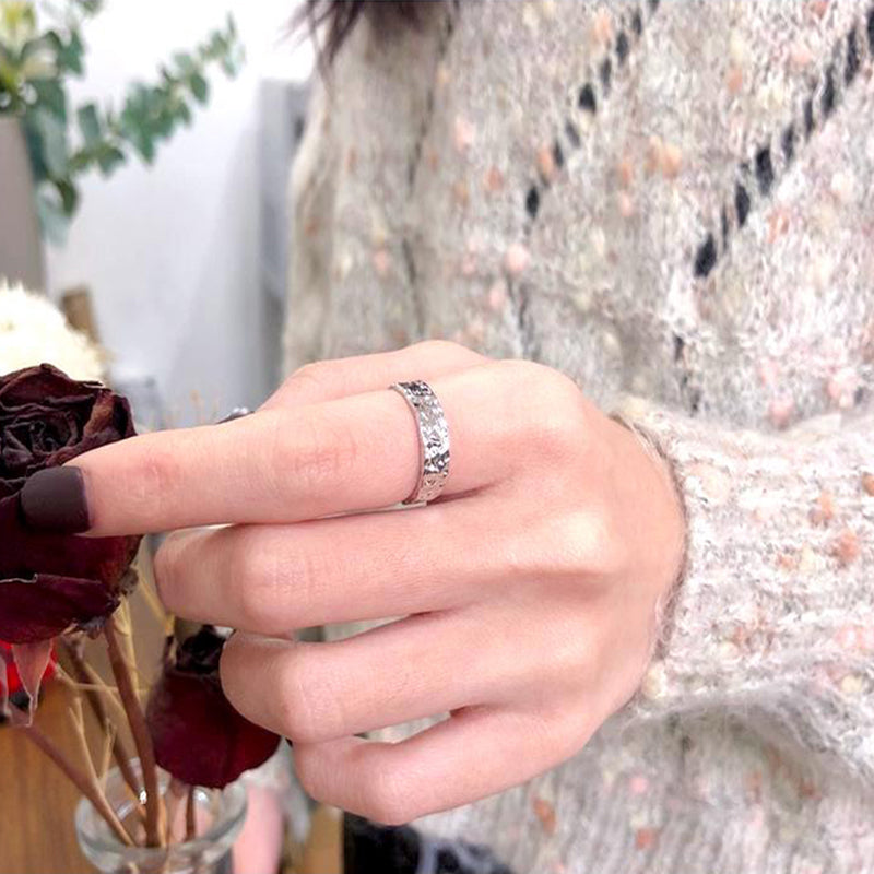 bague reliefs dorée argentée portée par une femme, vue en gros plan avec un pull texturé et des fleurs séchées en arrière-plan