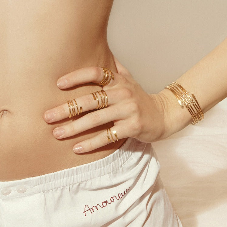 bague spirale dorée vanna sur main avec plusieurs anneaux empilés, bracelet assorti, portée proche de la taille blanche