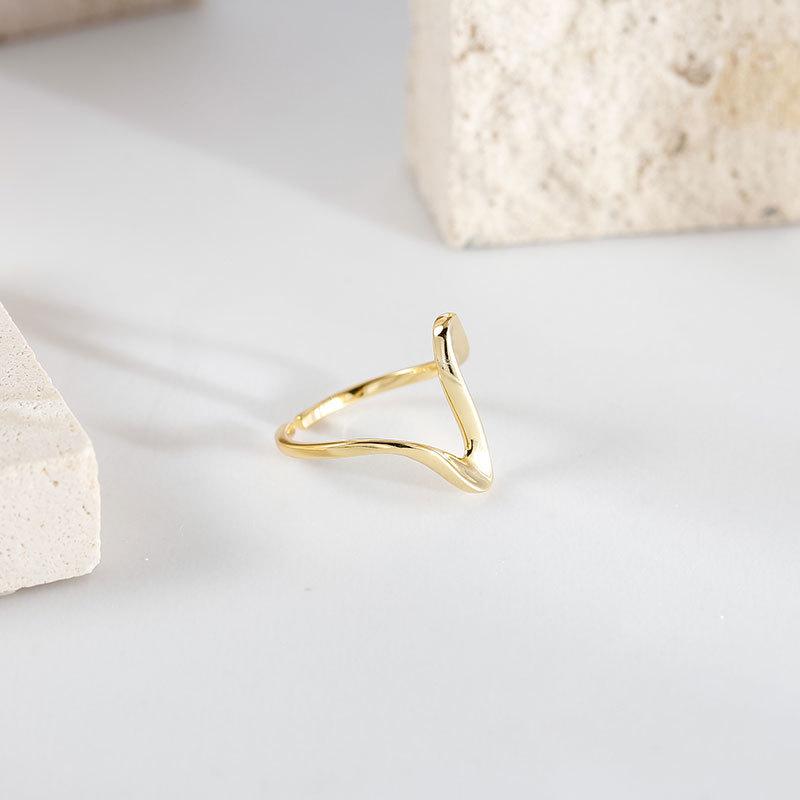 bague vague en métal doré et argenté, design élégant et minimaliste, posée sur un fond avec des blocs de pierre clair