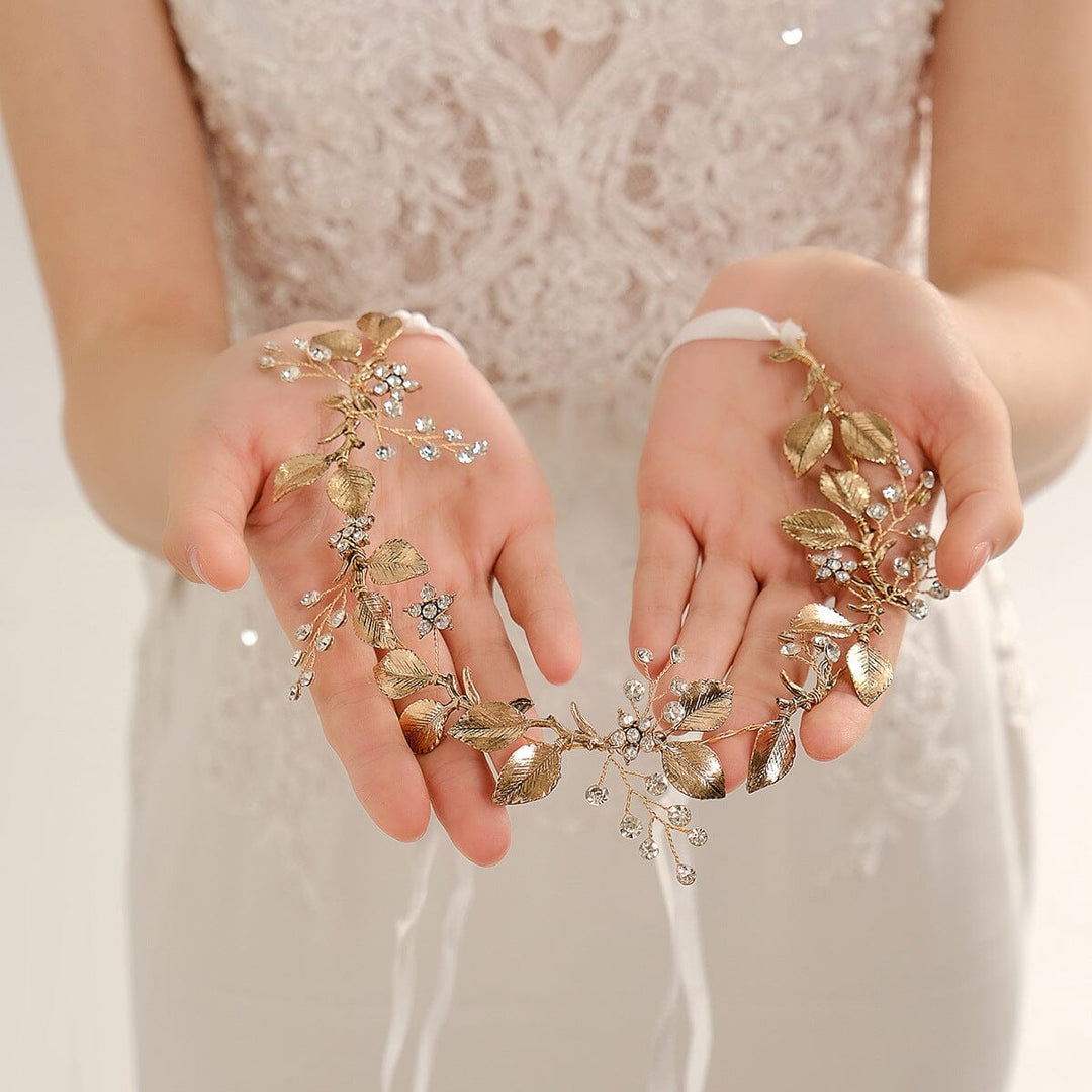 Accessoire cheveux doré avec fleurs cristallines pour mariage tenu dans les mains d'une mariée en robe blanche dentelle