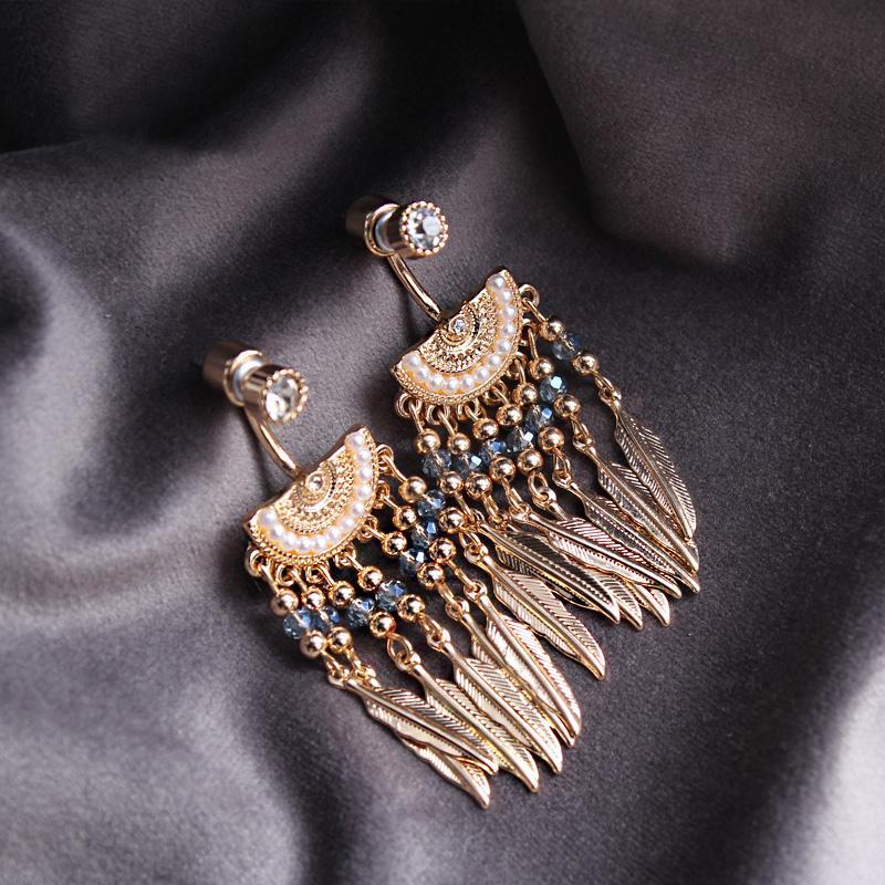 boucles d'oreilles plumes amérindiennes en or, ornées de perles et de pierres bleues, posées sur un tissu noir