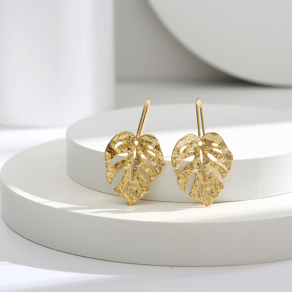 boucles d'oreilles feuille dorée en forme de feuille de monstera sur présentoir blanc, bijoux élégants et raffinés