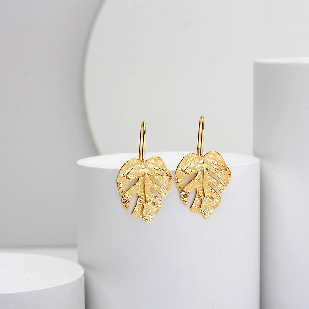boucles d'oreilles en forme de feuille dorée, élégantes et délicates, mises en avant sur un fond minimalist