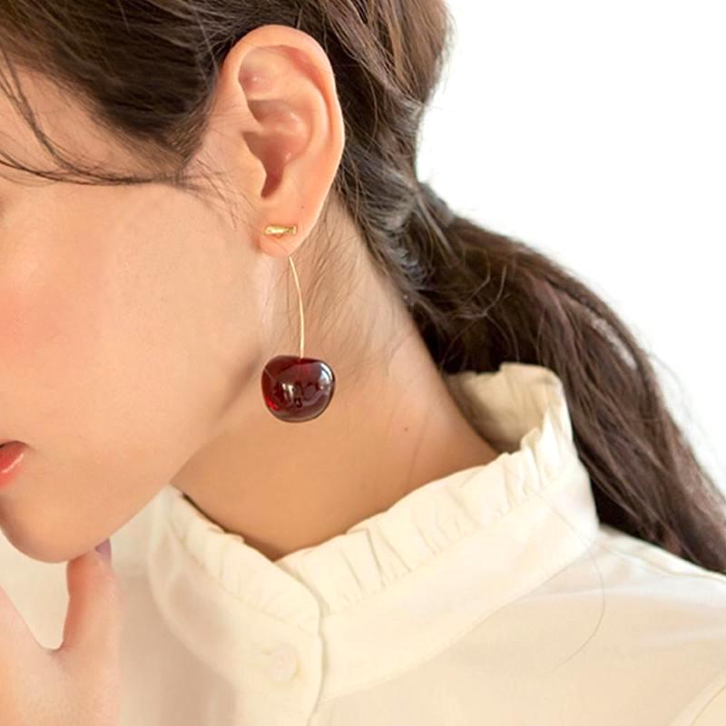 boucles d'oreilles cerise pendantes élégantes portées par une femme dans une chemise blanche, bijou tendance et original