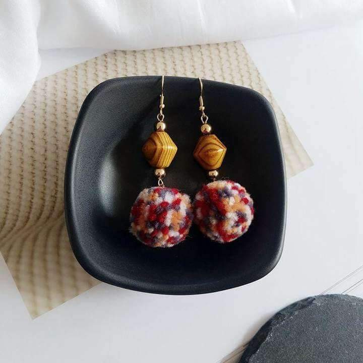 Boucles d'oreilles pompon multicolore avec ornements en bois dans une assiette noire, élégance et originalité.
