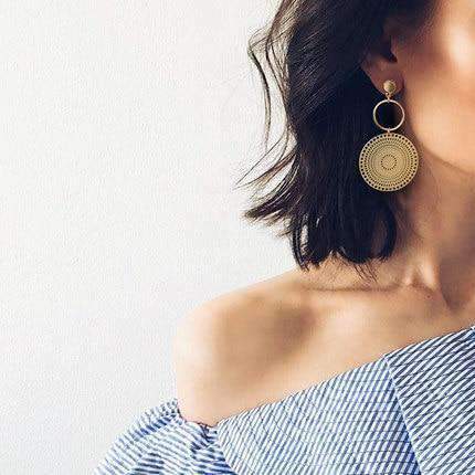 boucles d'oreilles ethniques chics en forme de soleil portées par une femme avec une blouse à rayures bleues