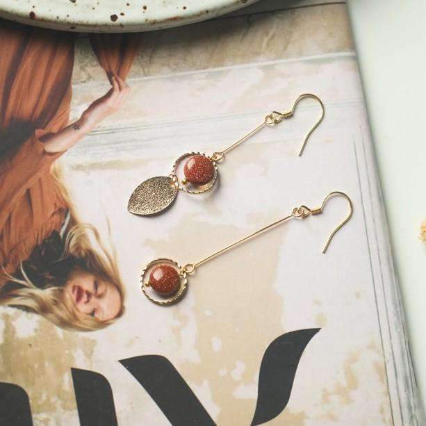 boucles d'oreilles pendantes dorées avec perles, délicatement posées sur un magazine féminin, parfaites pour un look chic