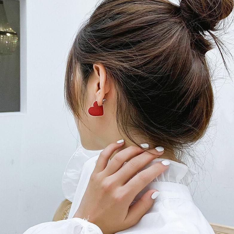 boucles d'oreilles cœur rouge portées par une femme avec un chignon et des ongles blancs montrant la boucle en gros plan