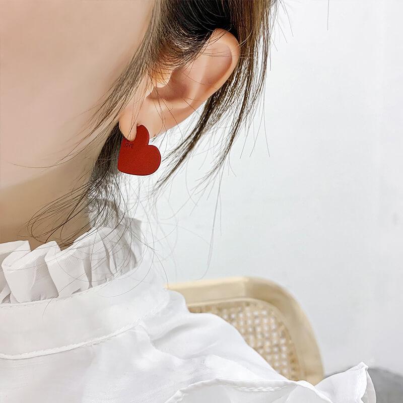 boucles d'oreilles cœur rouge en forme de cœur portées par une femme avec des cheveux attachés et une chemise blanche soyeuse