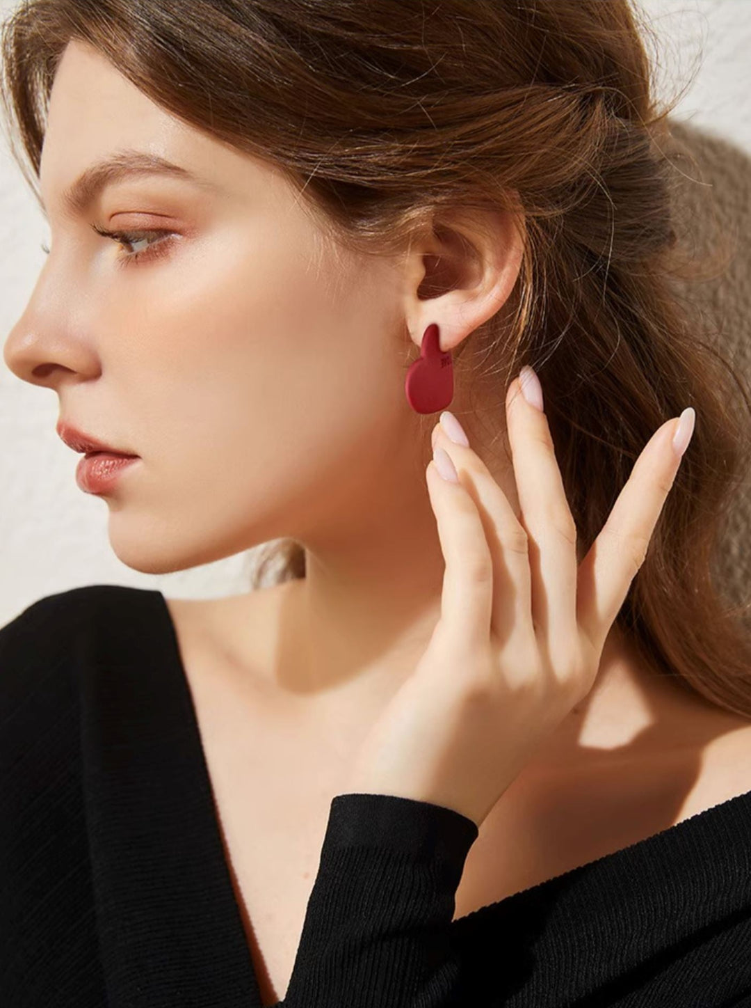 Boucles d’oreilles cœur rouge portées par une femme élégante portant un pull noir, détail sur le design épuré et chic
