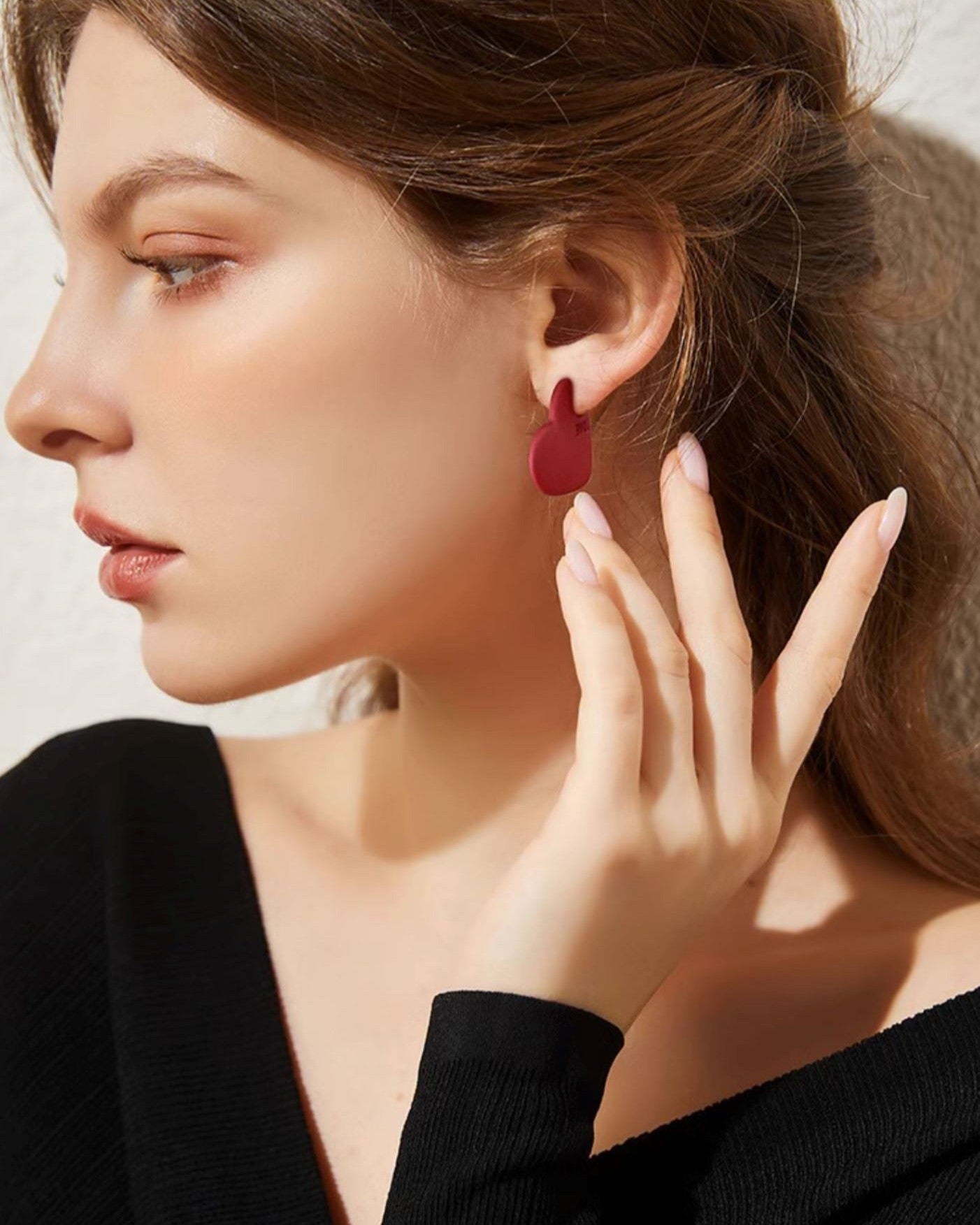 Boucles d’oreilles cœur rouge portées par une femme élégante portant un pull noir, détail sur le design épuré et chic