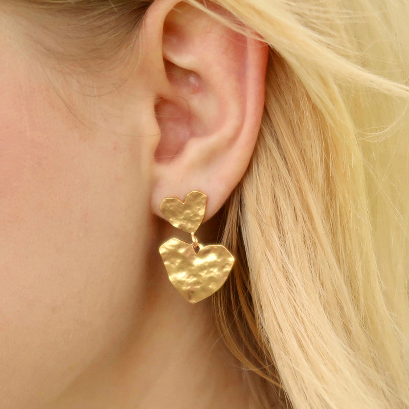 boucles d'oreilles en or en forme de cœur portées par une femme avec des cheveux blonds vue en gros plan sur son oreille