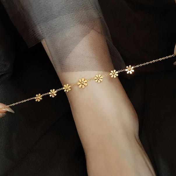 Bracelet de cheville doré avec des fleurs délicates porté sur une cheville, parfait pour un look élégant et féminin.