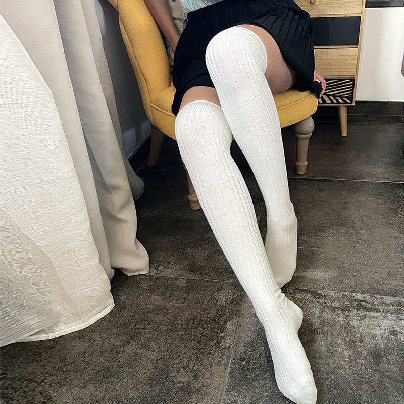 chaussettes hautes mi-cuisses femme laine et coton blanches, portées avec une jupe noire dans un intérieur chaleureux