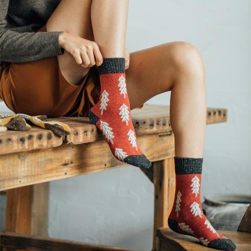 chaussettes de noël rouges avec motifs d'arbres blancs portées par une femme, parfaites pour l'hiver et les fêtes