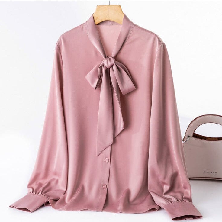 Chemise rose clair en satin avec noeud papillon, modèle Helene, présentée sur cintre, accompagnée d'un sac beige.