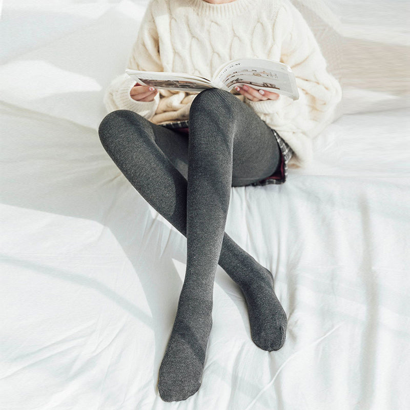 femme portant des collants molletonnés en cachemire pour hiver en lisant sur un lit blanc, confortables et chauds.