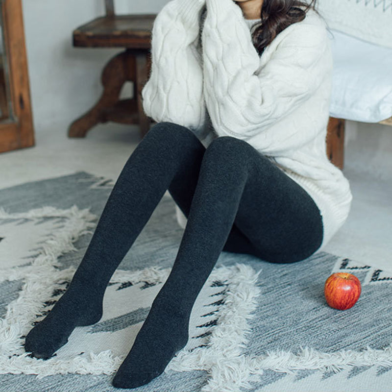 collant molletonné hiver en cachemire, femme en pull blanc et collants noirs, assise sur un tapis près d'une pomme rouge