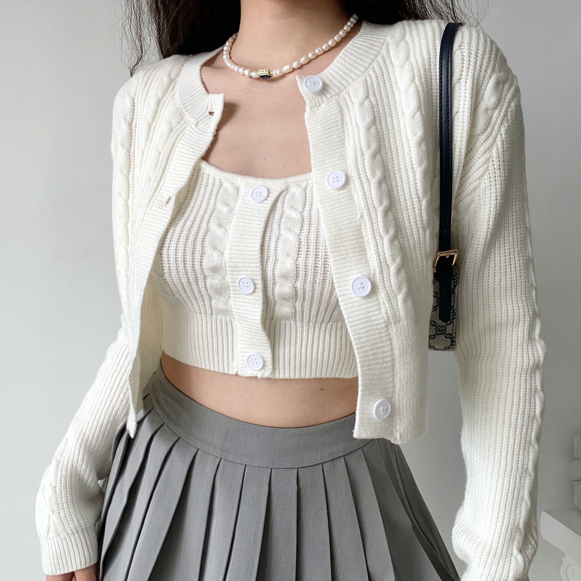 ensemble débardeur et gilet femme blanc en tricot à boutons porté avec une jupe plissée grise et un collier de perles