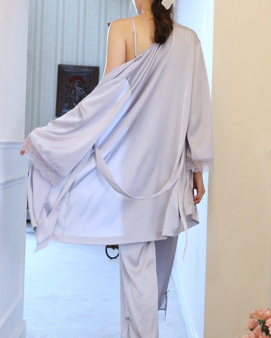 Ensemble de pyjama en satin pour femme, montrant une personne vue de dos portant un kimono de couleur pastel dans un intérieur chaleureux.